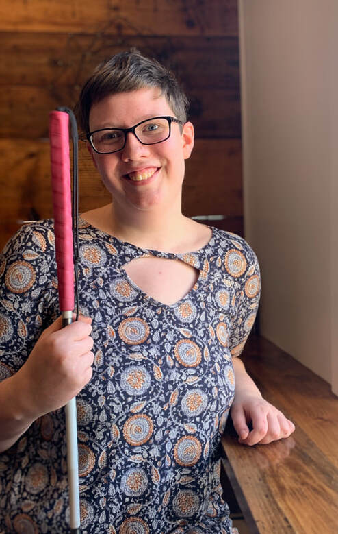 Woman with short hair, a paisley shirt, and a pink cane smiles at the camera